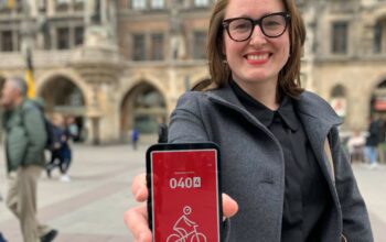 App-Anreize: Ein Mitmachsystem für erradelte Kilometer - Stadträtin Julia Bild hält ihr Smartphone auf dem Marienplatz in die Kamera