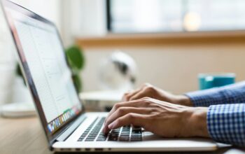 Nahaufnahme von einem Laptop. Eine Person, deren Hände man sehen kann, schreibt auf der Tastatur des Laptops.